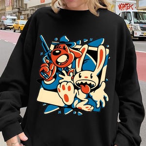 Può includere: Felpa nera con grafica a cartoni animati raffigurante un cane e un coniglio su sfondo blu e bianco. Il cane è rosso e il coniglio è bianco. La felpa è a girocollo.