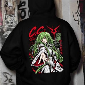 May include: A black hooded sweatshirt featuring a graphic print on the back of an anime character with long green hair, wearing a white outfit with black straps. The design includes red text reading C.C. and Code Geass, along with Japanese characters.