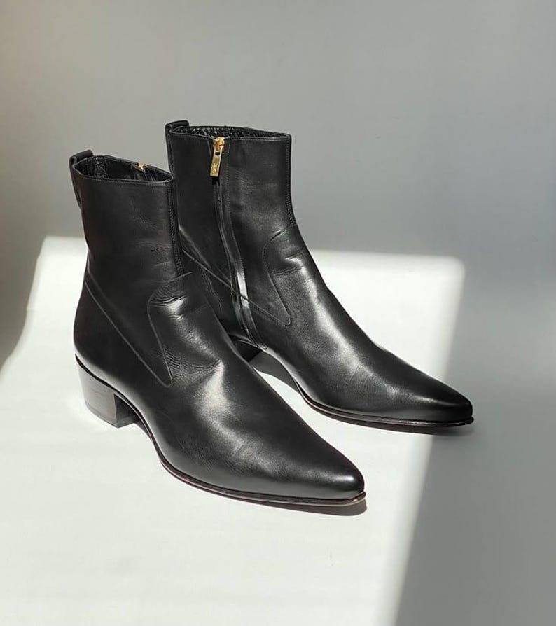 May include: A pair of black leather ankle boots with pointed toes and a low heel. The boots have a zipper closure on the side and a gold-colored zipper pull. The boots are displayed on a white surface.