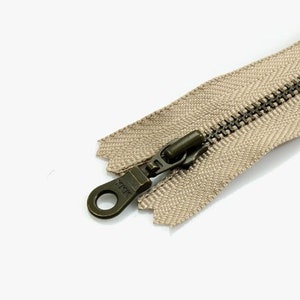 May include: Close-up of a beige zipper with a dark metal pull and teeth. The zipper is partially open, revealing the interlocking teeth. The fabric tape has a woven texture. Ideal for sewing projects.