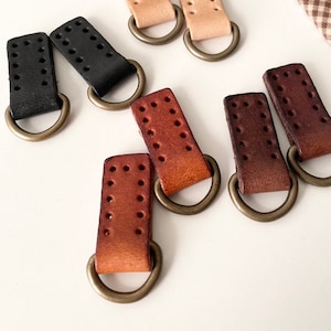 May include: Six leather strap loops with metal rings. Two are black, two are light brown, and two are dark brown.