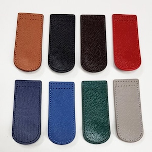 May include: An assortment of eight leather magnetic bookmarks in various colors. The bookmarks are rectangular with rounded bottoms and stitched edges. Colors include brown, black, dark brown, red, navy, blue, green, and gray.