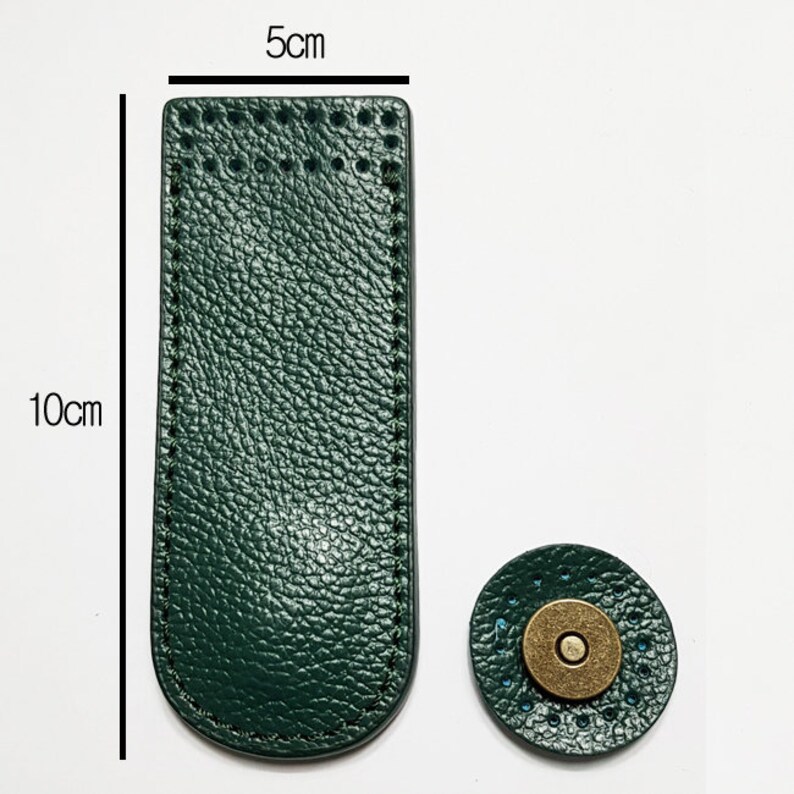 May include: Dark green leather magnetic snap closure, 10cm long and 5cm wide, with a matching circular piece. The leather has a textured appearance and is stitched around the edges. The circular piece has a brass-colored magnetic center.