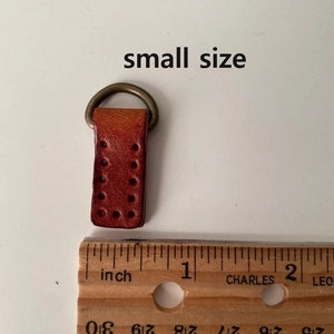 Puede incluir: Peque&ntilde;a correa de cuero marr&oacute;n rojizo con un anillo de metal color lat&oacute;n. La correa tiene varios agujeros peque&ntilde;os y espaciados uniformemente. El texto "small size" est&aacute; arriba. Una regla muestra unos 2,5 cm de largo.