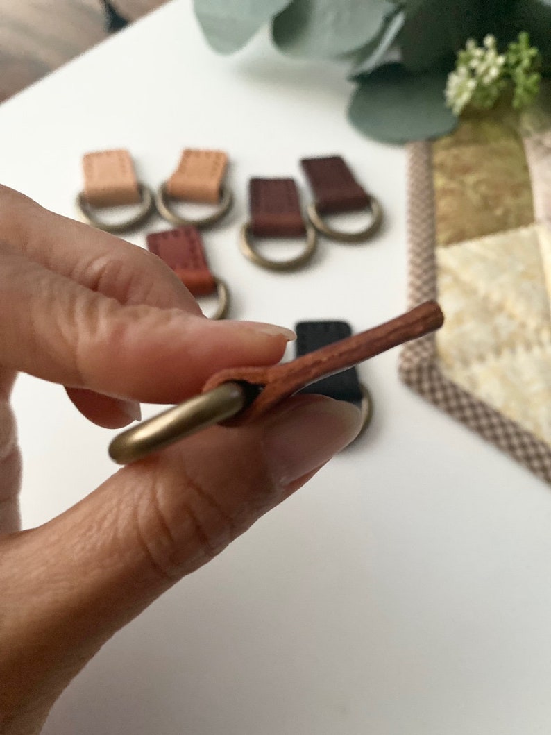 Puede incluir: Primer plano de varias leng&uuml;etas de cuero con anillos met&aacute;licos de color lat&oacute;n. Las leng&uuml;etas son de varios tonos de marr&oacute;n y beige. Una leng&uuml;eta se sostiene en la mano, mostrando el detalle del cuero y el anillo. El fondo est&aacute; borroso.