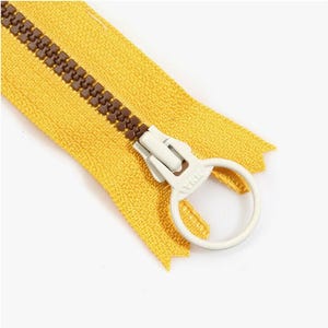 May include: Close-up of a yellow zipper with brown teeth and a white pull tab. The zipper is partially open, revealing the teeth and the fabric backing. The pull tab has a circular design.