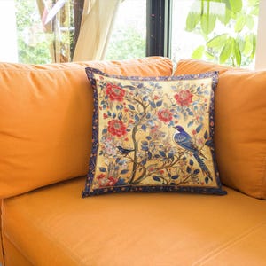 Puede incluir: Una almohada decorativa con un patrón floral que presenta pájaros azules y flores rojas sobre un fondo amarillo. La almohada tiene un borde azul oscuro.