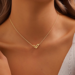 May include: A fine gold necklace with a small, open heart pendant. The pendant is embellished with tiny, sparkling details. The necklace is shown on a person's neck, emphasising the jewellery's design and elegance.
