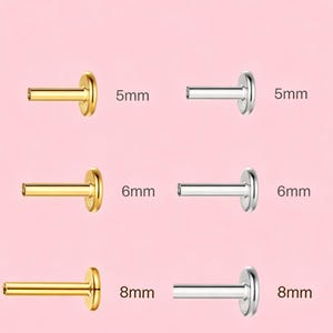 Può includere: Una selezione di labret in oro e argento. I labret sono disponibili nelle lunghezze di 5 mm, 6 mm e 8 mm. L'immagine è su uno sfondo rosa tenue.