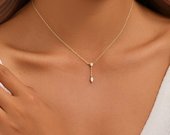 May include: A delicate gold necklace featuring a small round diamond and a teardrop-shaped diamond pendant. The necklace is suspended from a fine gold chain, creating a minimalist and elegant design. The jewelry is displayed against a neutral background.