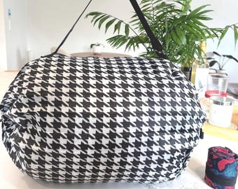 May include: A black and white houndstooth patterned reusable shopping bag with black straps. The bag is folded and rolled up.