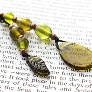 May include: A green and brown glass bead necklace with a silver leaf charm. The necklace is on a book with text about the Incas.