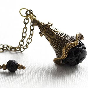 Könnte beinhalten: Eine goldene Kettenkette mit einem Anhänger aus schwarzem Lavastein. Der Anhänger ist blumenförmig mit einem detaillierten Design.