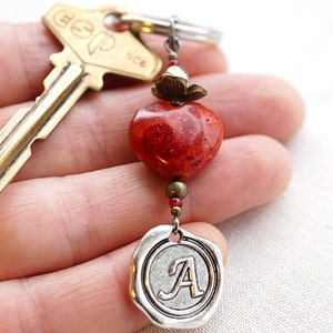 May include: A red coral heart charm with a silver charm with the letter A on it, attached to a brass key.