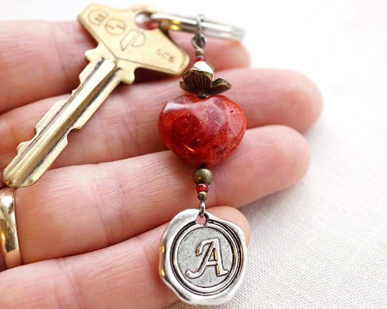 May include: A red coral heart charm with a silver charm with the letter A on it, attached to a brass key.