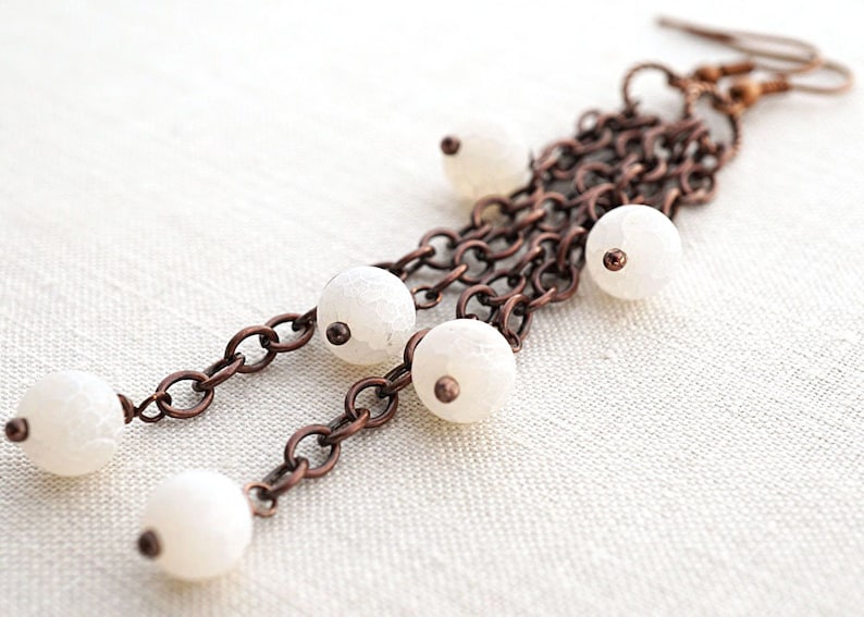 Pu&ograve; includere: Un paio di lunghi orecchini a catena di rame con perline di agata bianca. Gli orecchini hanno un design semplice ed elegante.