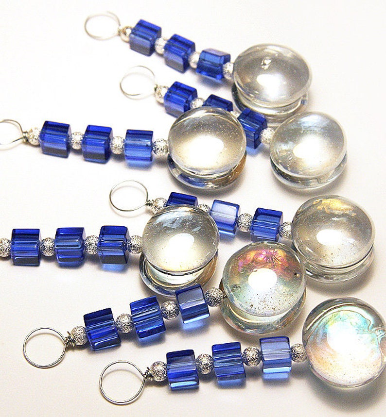 May include: Several decorative charms with a silver loop, clear glass orb, and blue square beads. The beads are strung together with silver-colored spacers. The orbs have a reflective, iridescent quality.