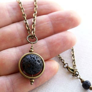 May include: A bronze chain necklace with a black lava rock pendant. The pendant is suspended in a bronze ring and spins freely.