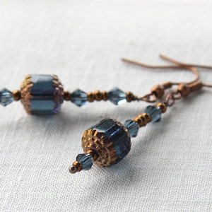 Può includere: Un paio di orecchini pendenti con perline blu e dorate. Gli orecchini sono realizzati con filo di rame e hanno una semplice chiusura a gancio.