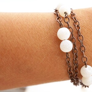 May include: A layered bracelet with white beads and a bronze chain.