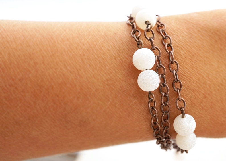 May include: A layered bracelet with white beads and a bronze chain.