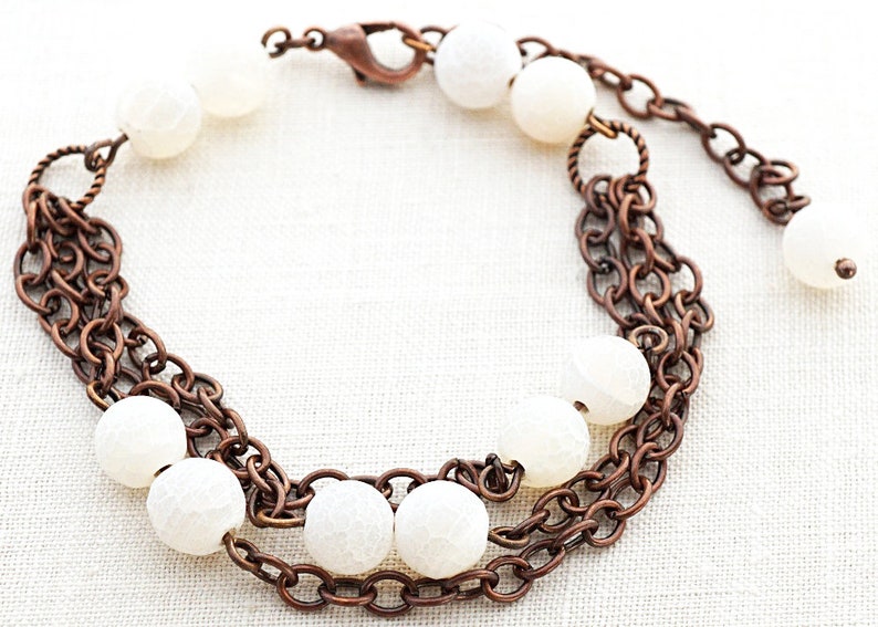 May include: A copper chain bracelet with white agate beads. The bracelet has a lobster clasp closure.