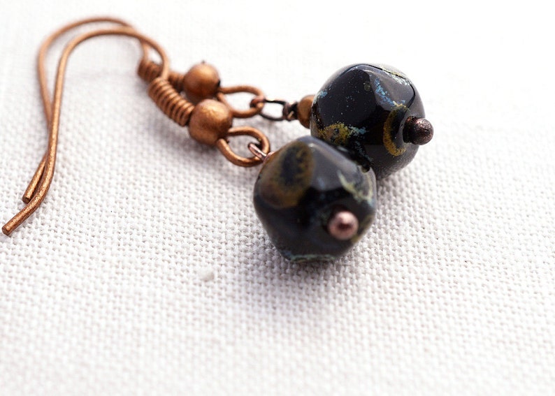 May include: A pair of earrings with black and gold patterned glass beads and copper wire accents.