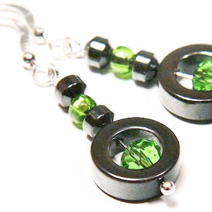 May include: A pair of black and green earrings with a silver hook. Each earring has a round black bead with a green crystal in the center.