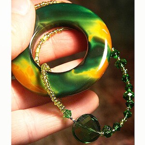 May include: A green and orange agate stone pendant with a hole in the center, strung on a green crystal beaded necklace.