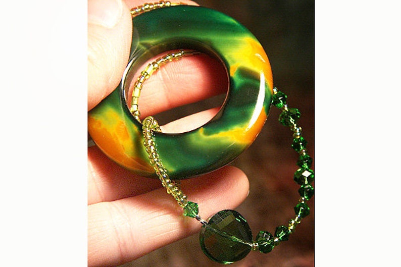 May include: A green and orange agate stone pendant with a hole in the center, strung on a green crystal beaded necklace.