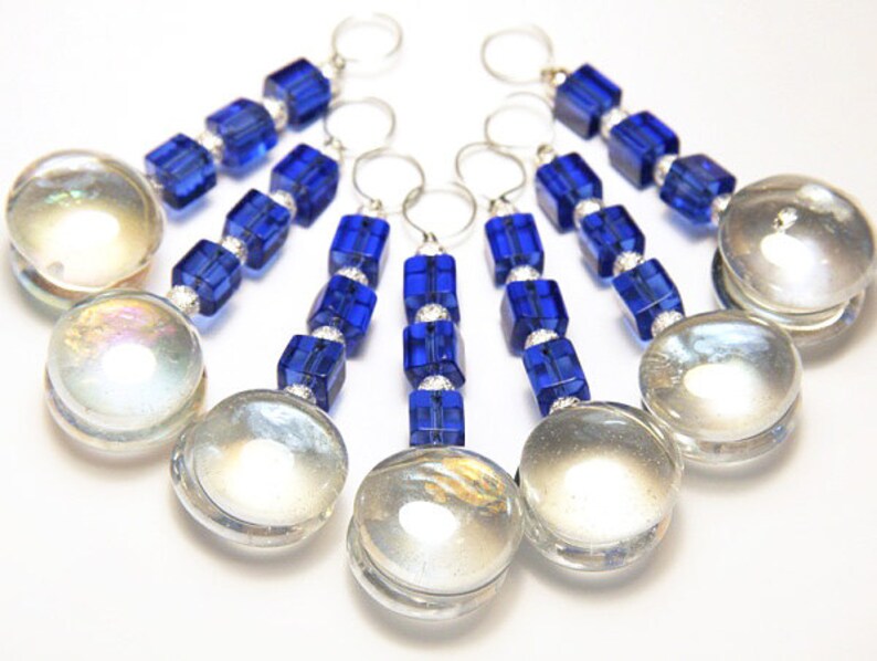 May include: A collection of six decorative keychains. Each keychain features a large, clear, iridescent glass orb, connected by a strand of blue, square beads and silver accents. The keychains have silver rings at the top.