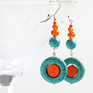 May include: Turquoise and orange dangle earrings with a silver hook. The earrings feature a turquoise circle with a smaller orange circle in the center.