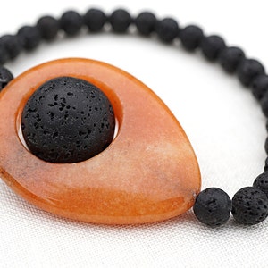 May include: A bracelet featuring a large orange stone with a black lava rock bead inside. The bracelet is made of black lava rock beads.