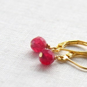May include: Gold earrings with red gemstone beads. The earrings have a simple design with a small, round bead hanging from a gold hoop.