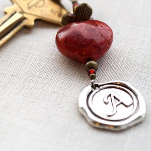 May include: A silver key chain with a red coral bead, a silver charm with the letter A, and a brass key with the word "Group" on it.