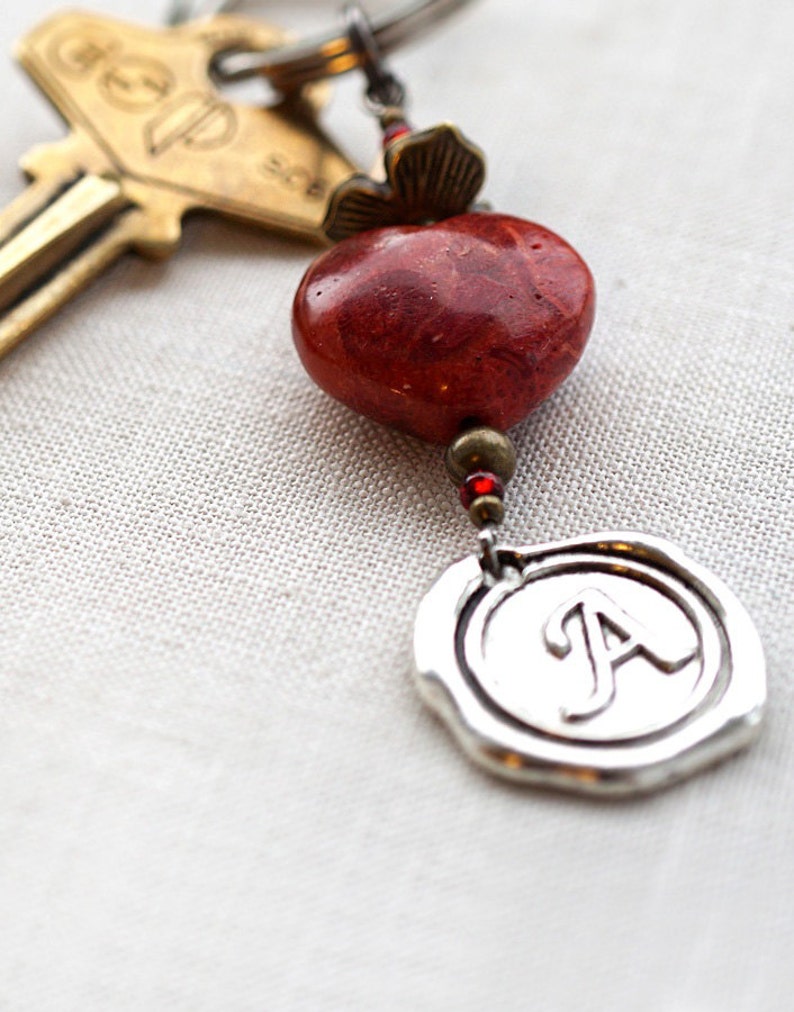 May include: A silver key chain with a red coral bead, a silver charm with the letter A, and a brass key with the word "Group" on it.