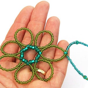 May include: A green and blue beaded flower pendant necklace. The flower is made of green beads and has a center circle of blue beads. The necklace is made of blue beads.
