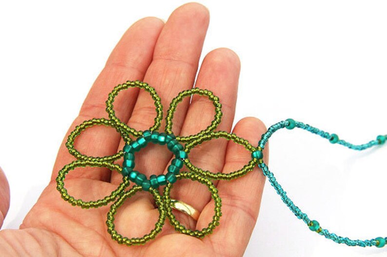 May include: A green and blue beaded flower pendant necklace. The flower is made of green beads and has a center circle of blue beads. The necklace is made of blue beads.