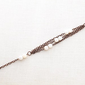 May include: A multi-strand bracelet with copper chains and white beads.