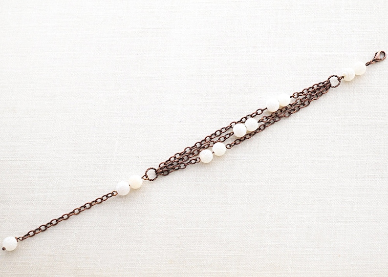 May include: A multi-strand bracelet with copper chains and white beads.