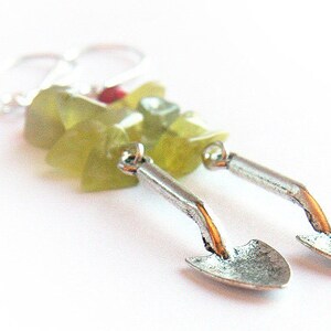 May include: A pair of silver earrings with a green and red stone design. The earrings are shaped like small shovels.