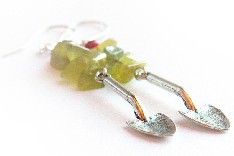 May include: A pair of silver earrings with a green and red stone design. The earrings are shaped like small shovels.