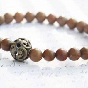 May include: A brown wooden beaded bracelet with a decorative metal charm. The bracelet is made of natural wood beads and features a unique metal charm with a swirling design.