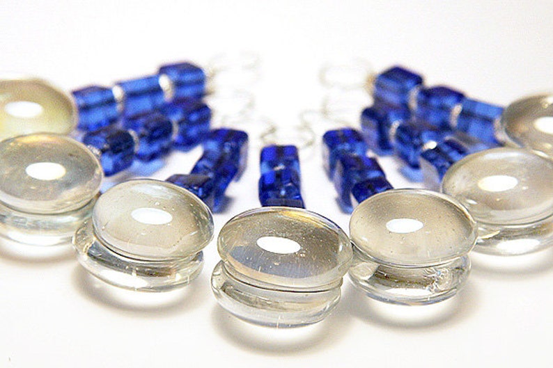 May include: Clear glass bottle stoppers with a circular design and a small white center. The stoppers are arranged in a semi-circle, with blue glass bead keychains in the background. The image is set against a white background.