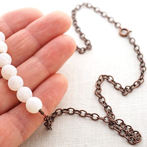 Pu&ograve; includere: Una collana di perle di agata bianca con una catena in rame. La collana &egrave; lunga circa 45 cm e ha una chiusura a moschettone.