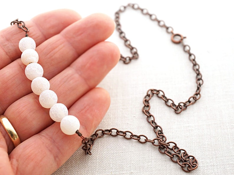 Pu&ograve; includere: Una collana di perle di agata bianca con una catena in rame. La collana &egrave; lunga circa 45 cm e ha una chiusura a moschettone.