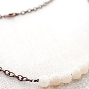Pu&ograve; includere: Una collana con catena di rame con una fila di perle di agata bianca.