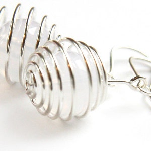 May include: Silver wire earrings with a clear crystal encased in a spiral cage design.