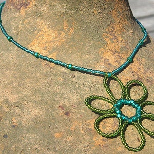May include: A teal blue beaded necklace with a green beaded flower pendant.