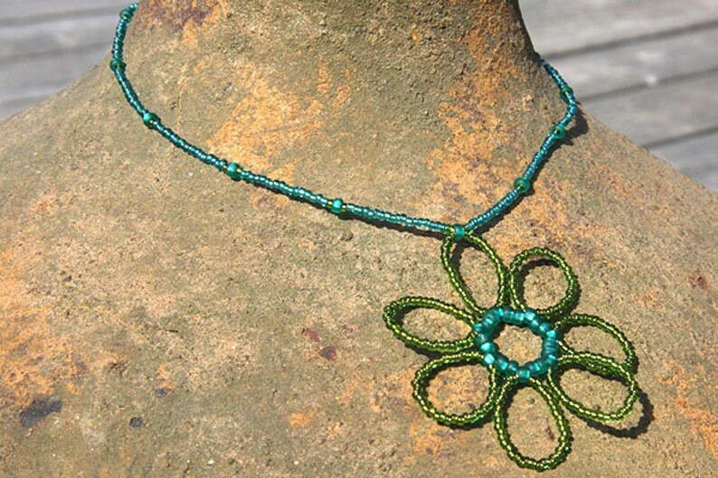 May include: A teal blue beaded necklace with a green beaded flower pendant.